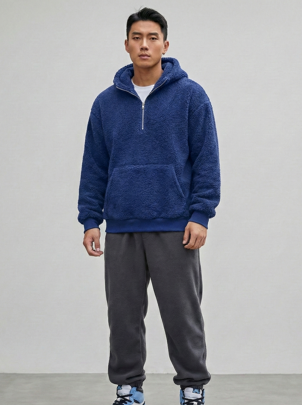 Person wearing a blue hoodie and gray sweatpants on a plain background